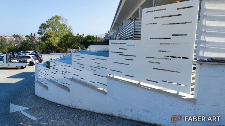 Recinzione moderna in lamiera bianca con fessure orizzontali montata su muretto esterno in pendenza
