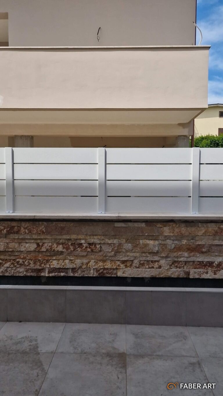 Recinzione moderna in ferro verniciato bianco fissata su un muretto rivestito in pietra.